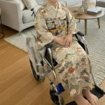 車いすに座ったまま綺麗に着用した着物（訪問着）姿の女性。福祉車いす着付けの仕上がり例。